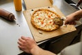 A pizzaiolo cuts a pizza with a round knife before wrapping it for delivery. Men& x27;s hands in front of the pizza.