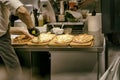 Pizzeria kitchen. Chef cook in apron and gloves cuts freshly baked pizza with roller knife