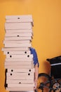 Pizzeria worker with blue uniform holding large stack of pizza delivering to client