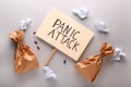 Placard with text PANIC ATTACK and paper bags on light background, top view