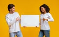Oyful interracial couple holding and pointing at blank advertisement placard Royalty Free Stock Photo