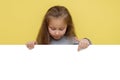 Place for your advertisement. Baby girl pointing to blank white billboard on yellow background, copy space. Emotions Royalty Free Stock Photo