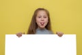 Place for your advertisement. Baby girl pointing to blank white billboard on yellow background, copy space. Emotions Royalty Free Stock Photo