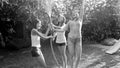 Plack and white image of cheerful laughing girls in wet clothes dancing under water from garden hose at house backyard Royalty Free Stock Photo