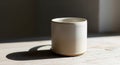 A plain, cylindrical ceramic mug sits on a light wooden surface, casting a distinct shadow to the Royalty Free Stock Photo