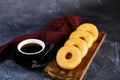 Plain Donuts with cup of black coffee served on wooden board isolated on napkin side view of baked food breakfast on table