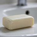 A plain, rectangular bar of soap rests on a white bathroom sink. The soap is off-white Royalty Free Stock Photo