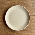 A plain, round ceramic plate in a soft beige color sits on a wooden surface. The plate Royalty Free Stock Photo