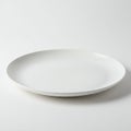 A plain, round, white ceramic plate is positioned on a white surface. The plate has a
