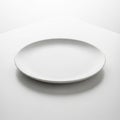 A plain, round white ceramic plate with a smooth surface sits centrally on a white, slightly Royalty Free Stock Photo