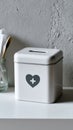 Plain tin tzedakah box with a simple heart icon, placed on a white surface, surrounded by utensils and a textured wall Royalty Free Stock Photo