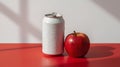 A plain white beverage can with condensation droplets sits beside a red apple on a red surface Royalty Free Stock Photo