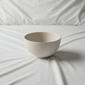A plain, white ceramic bowl is centered on a white, textured fabric surface, possibly a Royalty Free Stock Photo