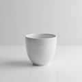 A plain white ceramic cup sits on a smooth, white surface. It has a simple, rounded Royalty Free Stock Photo