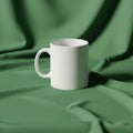 A plain white ceramic mug is centered on a soft, green, draped cloth backdrop Royalty Free Stock Photo