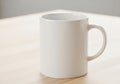 A plain white ceramic mug with a handle is placed on a light wooden Royalty Free Stock Photo