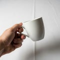 A plain white ceramic mug by its handle against a smooth light Royalty Free Stock Photo