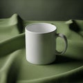 A plain white ceramic mug is positioned on a draped textured green fabric Royalty Free Stock Photo