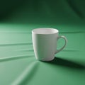 A plain white ceramic mug rests on a smooth green fabric surface Royalty Free Stock Photo