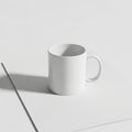 Plain white ceramic mug sits on a minimalist white surface, casting Royalty Free Stock Photo