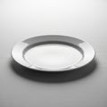A plain white ceramic plate is centered on a light gray, textured surface. The plate has Royalty Free Stock Photo