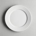 A plain white ceramic plate is centered on a textured, light gray surface. The plate is circular Royalty Free Stock Photo