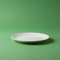 A plain white ceramic plate sits against a smooth green backdrop. The plate is round Royalty Free Stock Photo