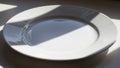 A plain white ceramic plate sits on a flat surface partially Royalty Free Stock Photo