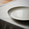 Plain white ceramic plate on a table covered with a light gray, textured fabric tablecloth Royalty Free Stock Photo