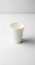 A plain white paper cup is centered on a smooth, white surface. The cup has a simple Royalty Free Stock Photo