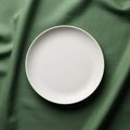 A plain white round plate is centered on a textured green fabric background. The plate i Royalty Free Stock Photo