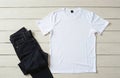Plain white tee shirt, dark blue denim jeans neatly placed on light timber planks. Unisex basic apparel presents clear empty Royalty Free Stock Photo