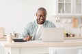 Plan finances. Positive african american mature man calculating taxes and using laptop computer, sitting in kitchen Royalty Free Stock Photo