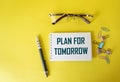 PLAN FOR TOMORROW, text in a notebook near glasses, a pen and paper clips