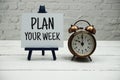 Plan Your Week text and alarm clock on white brick wall and wooden background Royalty Free Stock Photo