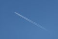 A plane crosses the blue sky diagonally leaving behind a double white trail Royalty Free Stock Photo