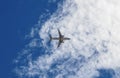 Bottom of white and silver plane heaing up in blue sky with scattered white clouds Royalty Free Stock Photo