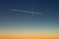 A plane flying in front of C/2020 F3, or Comet Neowise, in the early morning sky with a gradient from orange sun glow to blue nigh