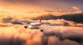 Plane is flying over mountains in low clouds at golden sunrise Royalty Free Stock Photo