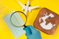 Plane model, face mask, loupe in hand and earth model on a yellow background. Hands in gloves. Flight impact of coronavirus COVID