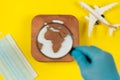 Plane model, face mask, loupe in hand and earth model on a yellow background. Hands in gloves. Flight impact of coronavirus COVID