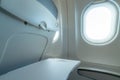 Plane window with white sunlight. Empty plastic airplane tray table at seat back. Economy class airplane window. Inside of