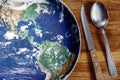 The planet Earth plate with a fork and knife on a wooden background. World hunger concept. Feed the world