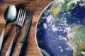 The planet Earth plate with a fork and knife on a wooden background. World hunger concept. Feed the world Royalty Free Stock Photo