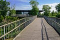 Plank-paved steel footbridge to building with glass wall in sunny summer afternoon