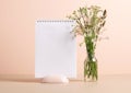 The planner's blank clean notepad stands on the table in vase with delicate green flowers. Mock up for text