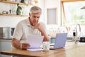 Planning, documents and finance with elderly man on laptop in a kitchen, reading retirement and savings plan in his home Royalty Free Stock Photo