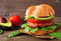 Plant based meatless burger with avocado, tomato and spinach against a wood background Royalty Free Stock Photo