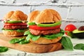 Plant based meatless burgers with avocado, tomato and spinach against a white brick background Royalty Free Stock Photo