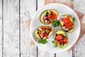 Plant based stuffed avocados with tomato bruschetta over white wood